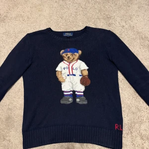 Polo Ralph Lauren tröja - Säljer denna riktigt snygga stickade tröjan från Polo Ralph Lauren med den klassiska PRL Björnen. Storleken är Large för juniorer, alltså 14–16 år. Den har använts några gånger men har inga defekter eller fläckar. Den är normal i passformen och sitter väldigt skönt. Den köptes för 3000 kr för endast ett år sen från Ralph Laurens hemsida.  Om du har några frågor eller prisförslag är det bara att skriva.