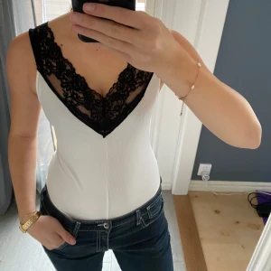 Vit ribbad body med spets - Säljer en vit ribbad linnetopp med djup v-ringning med svart spets. Helt ny endast testad 