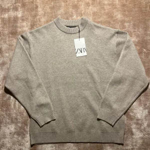 Beige stickad tröja från Zara - Snygg beige stickad tröja från Zara med rund hals och ribbade muddar vid ärmslut och nederkant. Enkel och stilren design som är lätt att matcha med dina favoritjeans eller sneakers. Perfekt för dig som gillar en clean och chill look.