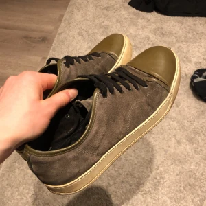 Lanvin sneakers i mocka och skinn - Lanvin sneakers med olivgröna skinn-tåpartier och grå mocka på sidorna. Svarta snören och vit platt sula med Lanvin-logga undertill. Snygg kontrast mellan material och färger, perfekt för dig som gillar stilrena men unika sneakers. Skorna tvättas självklart innan de säljs. Priset är absolut inte hugget i sten så kom med bud! Hör av er vid frågor 