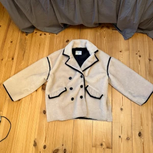 Pälsjacka  - Supermjuk och fluffig beige pälsjacka  i storlek XS, 32-34.. Jackan har svarta kontrastdetaljer, dubbelknäppning med svarta knappar och två fickor framtill. Perfekt för att hålla sig varm och snygg under kyliga dagar. Mycket bra skick!