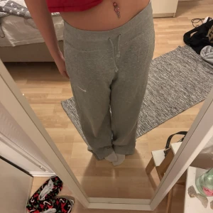 Grå mjukisbyxor från Nike - Säljer ett par grå mjukisbyxor från Nike med normal passform och bred resår i midjan. Byxorna har snörning framtill och ett litet Nike-logo broderat på vänster ben. Materialet är mjukt och skönt, perfekt för chill dagar. Modellen är loose och har raka ben.