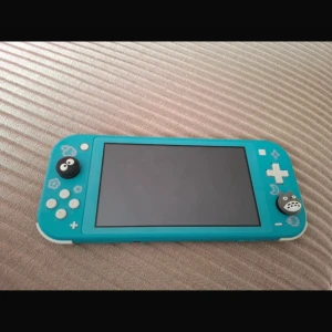 Nintendo Switch Lite Turkos - Nintendo Switch Lite i turkos färg, i fint skick utan synliga repor eller skador. Dekorerad med söta joystick-skydd och motiv på framsidan. Perfekt för portabelt spelande och kompatibel med alla Switch-spel. Ingår även laddare och ett fodral till enheten. 