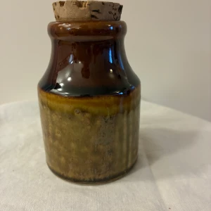 Krus i 60-talsstil - Keramikburk med korklock, cirka 10 cm hög och 6 cm i diameter. Burken har en brun och beige glasyr i gott skick utan synliga defekter eller slitage. Vet ej om den är från 60-talet eller bara innehar stilen. 