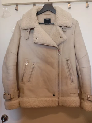 Beige teddyjacka från Bershka - Säljer en beige teddyjacka från Bershka med fluffig krage och foder. Jackan har flera dragkedjor, bälten vid ärmslut och nederkant samt en snygg oversized look. Perfekt för kalla dagar och riktigt mysig att ha på sig.
