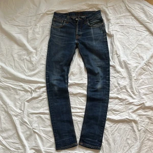 Blå Nudie Jeans  - Riktigt snygga Nudie Jeans med snygga slitningar • Finns en liten defekt under gylfen (syns på bilden), men märks inte vid användning • Modellen är grim tim men skulle säga att dem har blivit lite tightare och mindre efter användning • Längd: 101 cm Bredd runt smalben: 15 cm • Orginala storlek: 30/34 • Hör av er vid frågor!