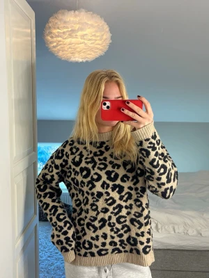 Beige leopardmönstrad stickad tröja - Säljer en beige stickad tröja med svart leopardmönster. Tröjan har rund halsringning, ribbade muddar och en loose passform. Perfekt för dig som vill ha en trendig och bekväm look med lite edge.