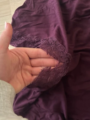 Lila långärmad topp med spets - Säljer en mörklila långärmad topp med v-ringning och dekorativ spets vid halsen. Toppen är mjuk och har en feminin touch med spetsdetaljer som gör den extra fin. Perfekt att styla med jeans eller kjol för en snygg look.Dock är spetsen lite sönder så ett billigare pris