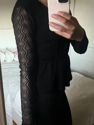Svart blus med spetsärmar från About You - Säljer en svart blus från About You med v-ringning och långa spetsärmar i zigzag-mönster. Blusen har en knytning i nacken och ett lätt rynkat parti vid midjan som ger en hour-glass form. Passa på!💗