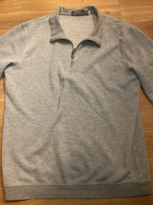 Grå half zip tröja från Polo Ralph Lauren - Snygg grå långärmad tröja från Polo Ralph Lauren med half zip och klassisk krage. Tröjan har en diskret broderad logga på bröstet och är gjord i mjuk bomull. Perfekt för chill dagar eller när du vill ha en clean look.