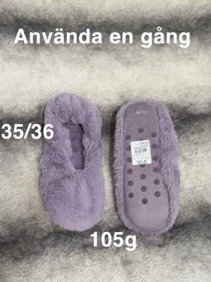 Lila fluffiga tofflor i storlek 35/36 - Supermjuka och fluffiga tofflor i lila färg, perfekta för att hålla fötterna varma hemma. De har en rund tå  med en mysig pälsliknande yta. Sulan har halkskyddande prickar för extra grepp.🌸 Använd en kort stund. Storlek 35/36