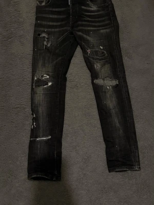 Svarta distressed jeans från Dsquared2 - Säljer ett par svarta jeans från Dsquared2 med coola slitningar. Jeansen har en skinny passform och är tillverkade i jeansmaterial med snygga detaljer och tvättad look. Perfekt för dig som gillar streetstyle och vill sticka ut.