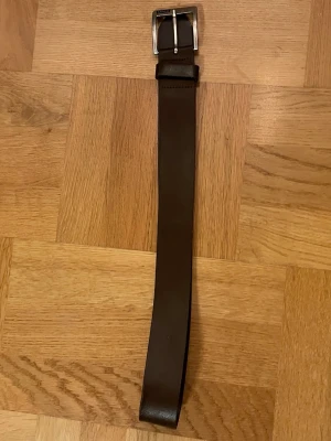Brunt skärp i skinn från Levi's - Säljer ett stilrent brunt skärp från Levi's i äkta skinn med klassisk metallspänne. Skärpet har en enkel design utan mönster och passar perfekt till jeans eller chinos. Storlek 74/28.alltså 70cm långt det är en Snyggt och tidlöst accessoar för din garderob.
