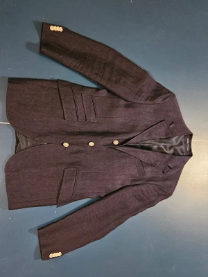 Mörkblå kavaj från Polo Ralph Lauren - Snygg mörkblå kavaj från Polo Ralph Lauren, tillverkad i Italien. Gjord i 100% linne med foder i cupro. Klassisk modell med tre knappar framtill, fickor med lock och dekorativa knappar vid ärmslut. Perfekt för dig som vill ha en stilren och tidlös look.