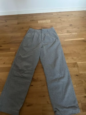 Grå kostymbyxor från Zara, storlek 38 - Säljer ett par grå kostymbyxor från Zara i storlek 38. Byxorna har rak passform, bälteshällor och pressveck framtill. Materialet känns mjukt och har en klassisk look som funkar till många olika stilar. Perfekt för dig som gillar stilrena och enkla plagg.