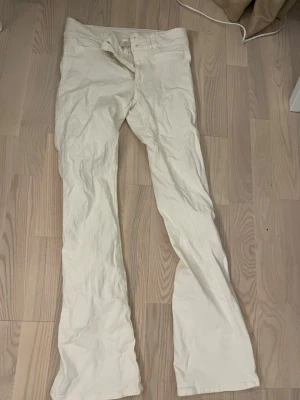 Vita bootcut byxor från H&M - Säljer ett par vita bootcut-byxor från H&M i storlek 170/20. Byxorna har låg midja och justerbar midja för bästa passform. Tillverkade i mjuk bomull med klassisk femficksdesign och dragkedja. Perfekta för dig som gillar en clean och enkel look.