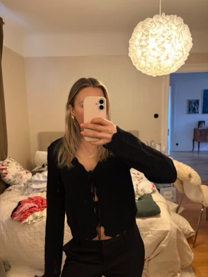 Svart stickad kofta med knyt - Säljer en svart stickad kofta med v-ringning och knyt framtill. Koftan är croppad och har långa ärmar. Ger en snygg siluett. Enkel men ändå trendig detalj till din outfit. Den är i storlek L men skulle säga att den passar s. Endast använd 1 gång. 