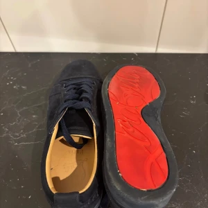 Mörkblå mockasneakers Christian Louboutin - Snygga mörkblå sneakers från Christian Louboutin i mjuk mocka med klassisk röd sula och diskret broderad logga på hälen. Skorna har rund tå, platt sula och mörkblå snörning. Insidan är ljusbeige och de kommer med originalkartong och dustbag. Skriv vid frågor, vid snabb affär kan priset diskuteras!!