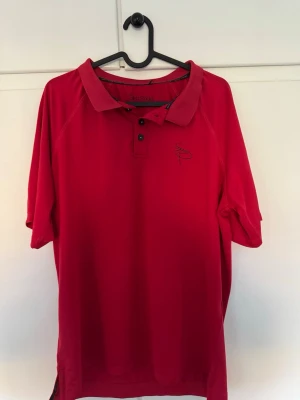 Röd polotop Silva Padel - Säljer en röd polotopp från Silva Padel med korta ärmar och krage. Toppen har knappar framtill och ett svart broderat SP-logotyp på bröstet. Materialet är lätt och andas, perfekt för sport och träning. Snygg och sportig design som sticker ut på banan.