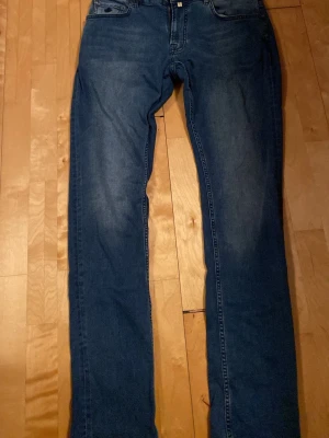 Morris Steve Satin Jeans blå 33/34 - Blå jeans från Morris, modell Steve Satin Jeans. Klassisk femficksdesign med snygga detaljer och mörkblå tvätt. Märkespatch i brunt skinn baktill och diskret broderad bakficka. Materialet är jeans med en mjuk känsla.