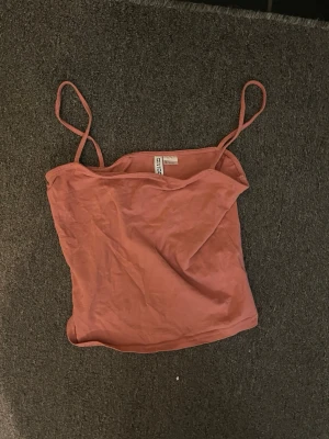 Rosa linnetopp från Gina Tricot - Säljer en enkel och snygg rosa linnetopp från Gina Tricot med tunna axelband. Toppen är ärmlös och har en rak, croppad passform som passar perfekt till sommaren. Materialet är mjuk bomull och färgen är en varm rosa ton.
