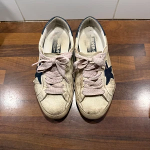 Golden Goose sneakers med blå stjärna - Säljer ett par klassiska Golden Goose sneakers i vitt skinn med blå stjärna på sidan och blå häl. SKOSNÖRERNA INGÅR INTE. Jag kan däremot skicka med original skosnören. Det finns hål i bak på båda skorna och ett på sidan som går att laga om man vill💗KAN GÅ NER I PRIS VID EN BRA AFFÄR☺️