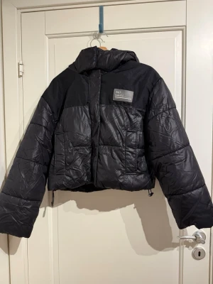 Kort dunjacka  - Svart kort dunjacka från bershka. Har muddar i ärmarna och luva, går även att snöra åt nedtill.