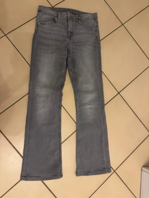 Grå bootcut jeans med raka ben - Snygga grå jeans med bootcut och raka ben. Klassisk femficksmodell med bälteshällor och dragkedja. Jeansen har en tvättad look och är tillverkade i mjukt denim-material som ger en skön känsla. Perfekt för dig som gillar stilrena och avslappnade jeans.