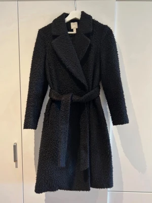 Svart kappa  - Svart kappa från H&M i storlek 36. Jackan har en fluffig och mjuk yta, bred krage och knyts med ett bälte i midjan. 