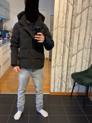 Canada goose Wyndham  - Svart pufferjacka från Canada goose med huva och diskret logga på ärmen. Jackan har dragkedja och knappar framtill, samt två sidofickor. Den är tjock och har en schysst oversized passform som är perfekt när det är kallt ute. Helt ny. Taggar och canadagoose påse medföljer. SISTA PRIS JAG GÖR ÄR 2700 inte mindre.