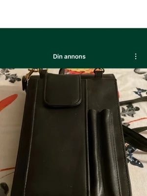 Svart axelväska i skinn med fack - Säljer en svart axelväska i skinn med flera praktiska fack och kortplatser. Väskan har ett lock med guldfärgat vridlås och en justerbar axelrem. Perfekt för dig som vill ha ordning på kort, mobil och småsaker. Stilren och enkel design. Säljs på fler sidor.