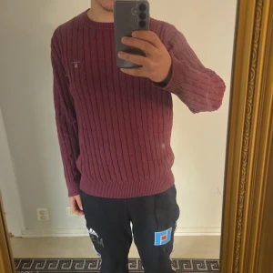 Vinröd kabelstickad tröja GANT XL - Säljer en vinröd kabelstickad tröja från GANT i storlek XL/L. Tröjan har rund hals, ribbade muddar och GANT-logga broderad på bröstet. Perfekt för dig som gillar klassisk stil med lite preppy känsla. Materialet är mjukt och stickat, passar bra till jeans eller chinos.