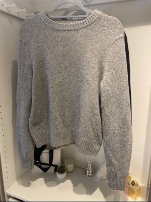 Grå stickad tröja från H&M - Säljer den trendiga grå stickade tröjan från H&M med rund halsringning och ribbade muddar vid ärmslut och nederkant. Helt oanvänt 