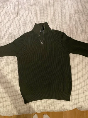 Mörkgrön stickad tröja med half zip - Säljer en mörkgrön stickad tröja med ribbad struktur och hög krage. Tröjan har en snygg half zip-dragkedja framtill och långa ärmar. Perfekt för dig som gillar stilrena och bekväma plagg med lite edge.Large men passar även medium. Priset kan diskuteras.
