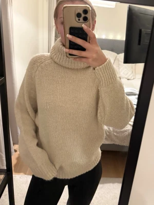 Beige stickad polotröja - Mysig och oversized beige stickad polotröja med bred krage. Tröjan har långa ärmar och ribbade muddar vid ärmslut och nederkant. Perfekt för kalla dagar och enkel att styla med jeans eller leggings.