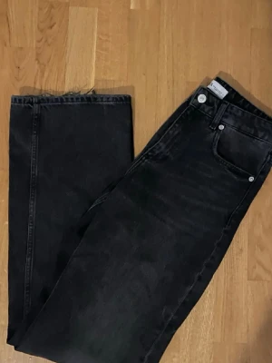 Svarta wide jeans från Zara - Säljer ett par svarta jeans från Zara med breda ben och klassisk femficksdesign. Jeansen har medel midja och rå kant längst ner på benen för en cool, avslappnad vibe. Materialet är robust denim i bomull. /midwaist