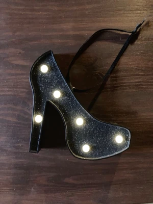 Klack sko i ljus - En liten klacksko med mått 13 x 13 cm, svagt ljus i gul nyans. Kräver AA batterier och hr svart glitter på ytan. Knappt använd och perfekt för en nattlampa eller något mjukt och mysigt ljus i bakgrunden 