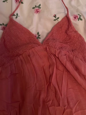 Rosa kortklänning från Pull&Bear - Supersöt rosa klänning från Pull&Bear i storlek S, liten i storlek. Klänningen har smock upptill, tunna axelband och ett flowigt, lätt tyg med volangdetalj längst ner. Använd en gång.