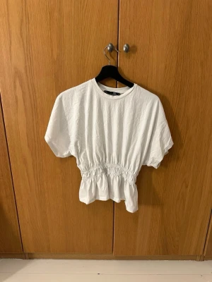 Vit fin topp - Säljer en vit topp från lager 157. Toppen har korta ärmar, rund hals och resår i midjan som ger en snygg volang nedtill. Storlek S. Bara att skriva vid frågor☺️