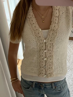 Beige stickad kofta från Zara - Superfin beige stickad kofta från Zara med korta ärmar och v-ringad hals. Koftan har virkade blomdetaljer. 