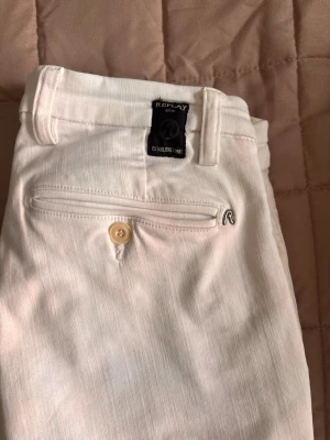Vita Replay Hyperflex jeans - Säljer ett par vita Replay Hyperflex jeans med klassisk femficksdesign och snygga detaljer som metallknapp och logotyp vid bakfickan. Stretchigt material för extra komfort och passform. Perfekt för dig som gillar stilrena och fräscha jeans.