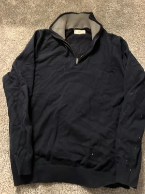 Mörkblå half zip tröja från MNG - Snygg mörkblå långärmad tröja från MNG med halv dragkedja i halsen och grå insida på kragen. Perfekt för dig som gillar enkel och stilren design. Materialet känns mjukt och bekvämt, och passformen är normal. Passar dig som vill ha en klassisk look.