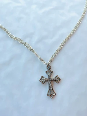 By prisförslag- dubbelt silvrigt halsband 45 cm kors diamanter  - Snyggt halsband med ett korsformat hänge, dekorerat med små glittrande stenar och en dubbel tunn silverfärgad kedja. 