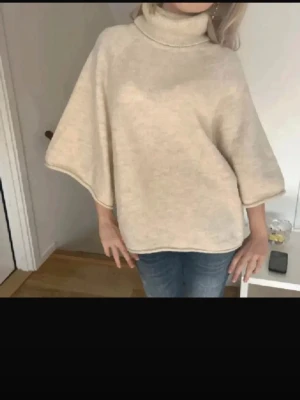 Beige polotröja med vida ärmar - Säljer en beige polotröja med breda, lösa ärmar och hög krage. Tröjan har en avslappnad passform och är stickad i mjukt material, perfekt för kyliga dagar. Enkel och stilren design som är lätt att matcha med jeans eller leggings.