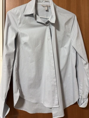 Ljusblå skjorta med klassisk krage - Snygg ljusgrå skjorta från H&M med klassisk krage och långärmad design. Skjortan har en rak passform och knappar framtill. Tillverkad i mjuk bomull som känns skön mot huden. Perfekt för dig som gillar stilrena och enkla plagg.