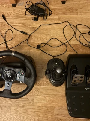 Logitech G920 Driving Force Racing Wheel & Pedals - Komplett Logitech G920 racing set med ratt, pedaler och växelspak. Passar Xbox och PC. Ratten har knappar för Xbox, pedalerna är i metall och allt ser ut att vara i mycket gott skick utan synligt slitage. Perfekt för realistisk racingupplevelse hemma.