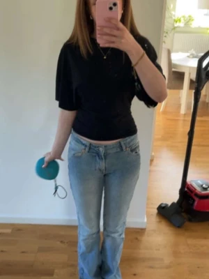 Svart figursydd topp - Säljer en svart topp med korta ärmar och rund hals. Modellen är lite loose och har en enkel, stilren design som passar till jeans eller kjol. Perfekt för dig som gillar minimalistisk stil och vill ha en basic topp i garderoben. Toppen är figursydd i midjan med passande större modell i armarna.