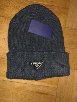 Prada mössa  - ❄️ Vintern är här, och vad passar bättre än en lyxig grå Prada-mössa? Denna ikoniska accessoar kombinerar värme med högsta mode. 🌟 Perfekt för både vardag och fest, den grå nyansen gör den lätt att matcha med vilken outfit som helst. 🔥 Investera i din stil – skaffa din Prada-mössa nu och gör ett statement! 👌