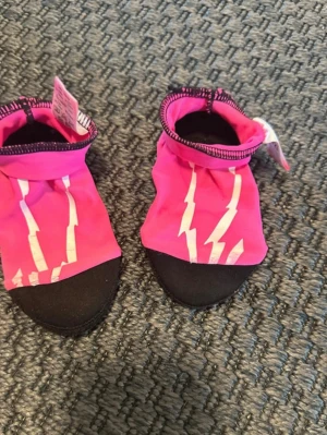 Barn Rosa badskor st20/21 - Säljer ett par coola rosa badskor. Skorna har svart platt sula och är gjorda i syntetmaterial som torkar snabbt. Perfekta för stranden eller poolen och har en mjuk, flexibel passform. 