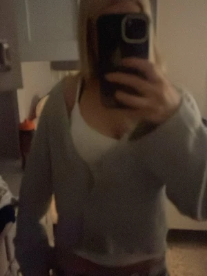 Ljusgrå kofta med knappar - Mysig ljusgrå kofta med knappar framtill och v-ringad hals. Koftan har en loose passform och långa ärmar, perfekt att slänga på sig över ett linne. Enkel och stilren design som funkar till många outfits.passar xs S 